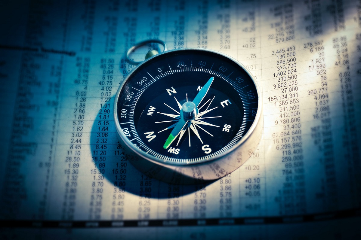 Image of a compass on top of a stock exchange sheet.