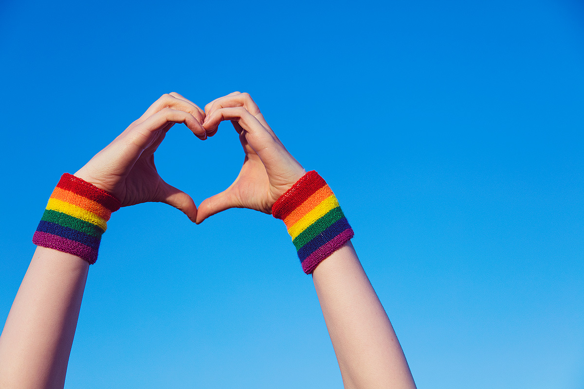 Hand making a heart sign with gay pride LGBT rainbow flag wristband