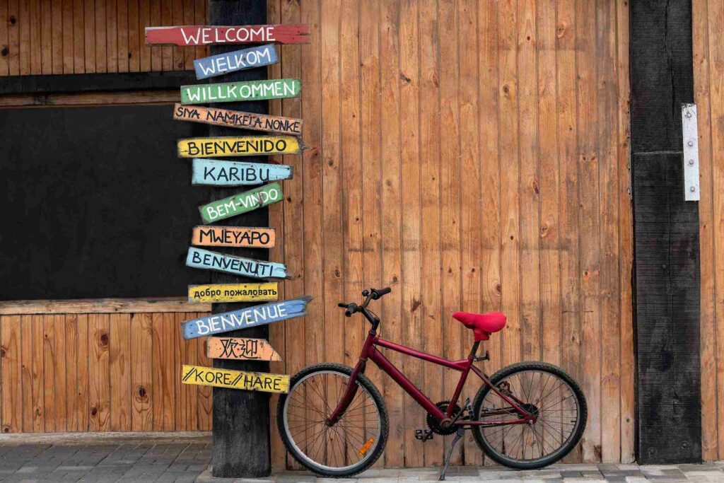 A red bike is propped up next to a tall sign that reads "welcome" in many languages.