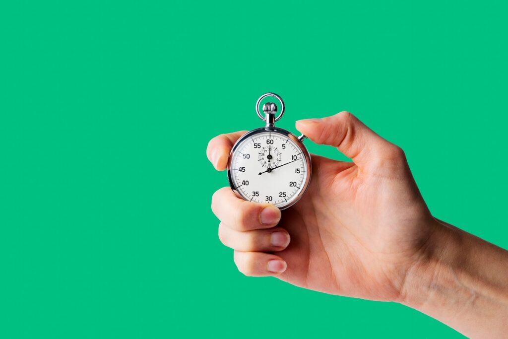 A hand holds a stopwatch in front of a bright green background