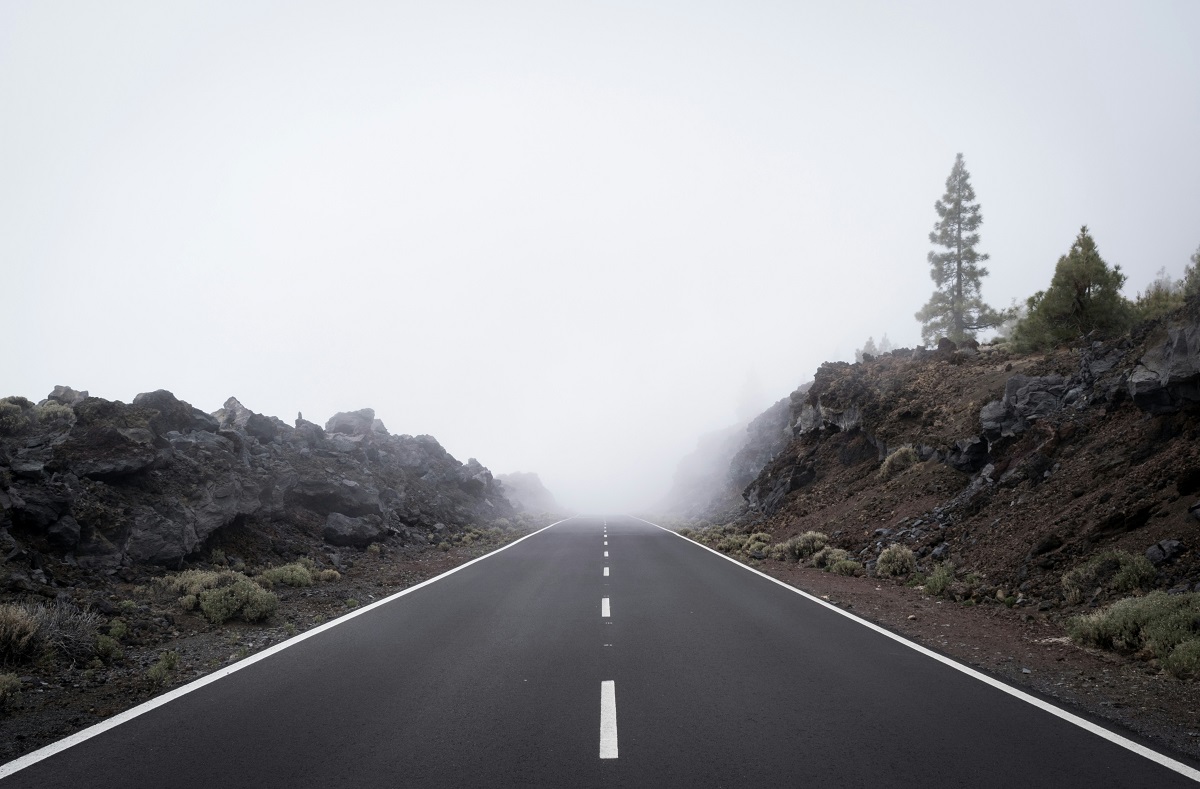 A paved road leads into dense fog.