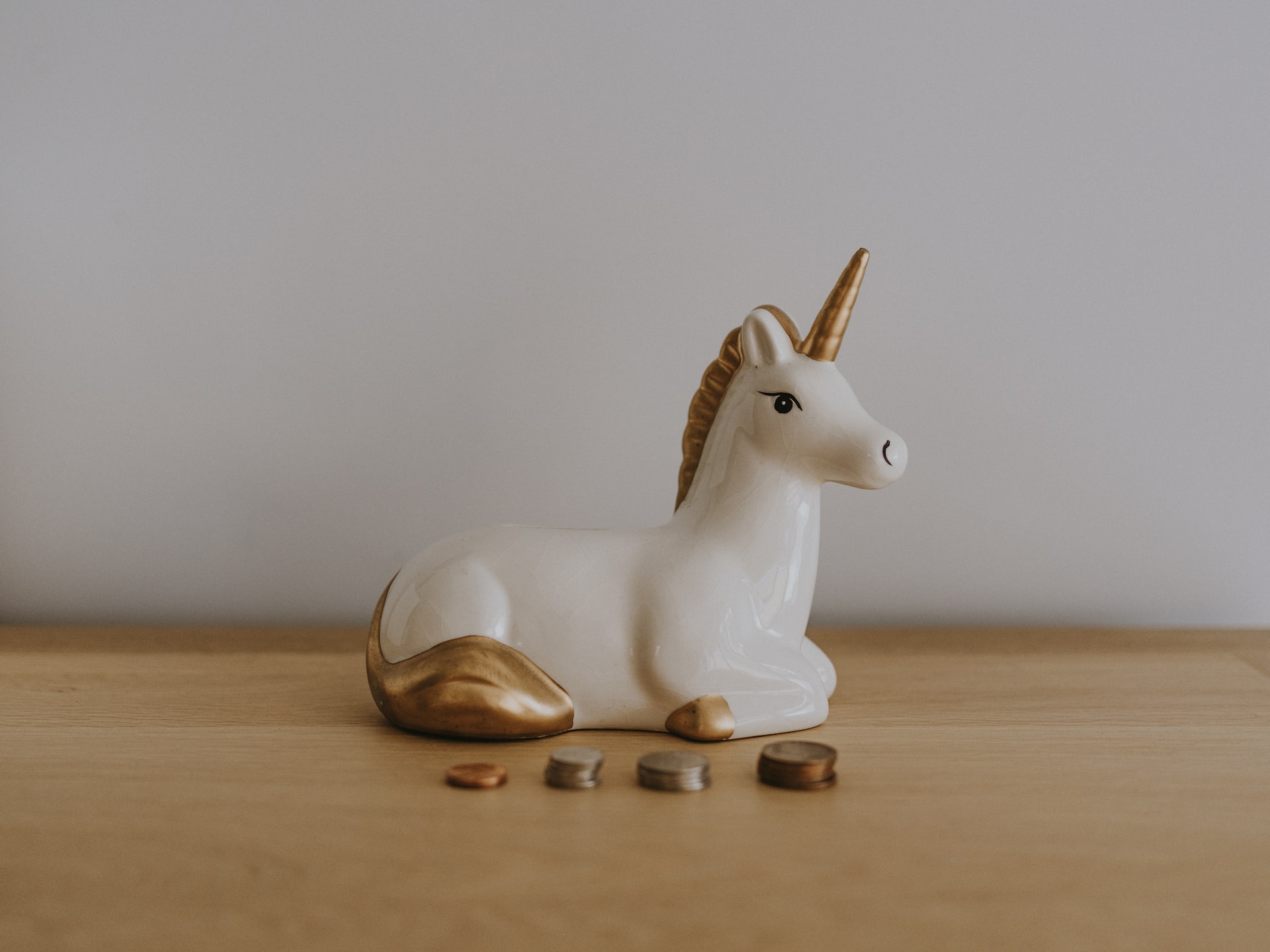 A ceramic unicorn sitting on a desk in front of stacks of coins.