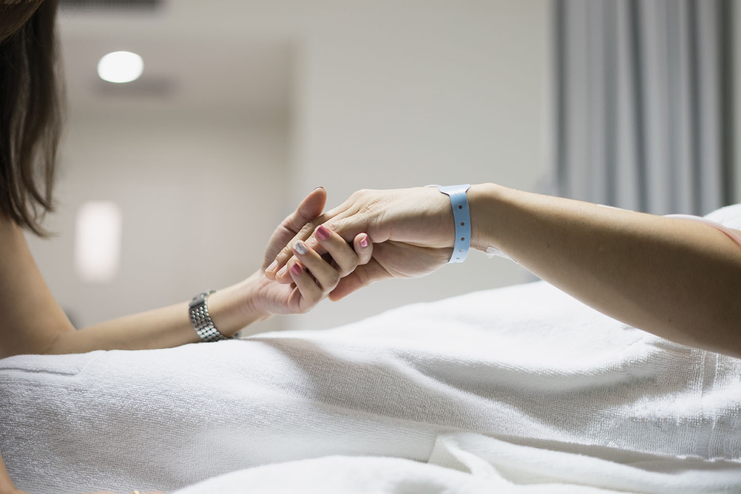 hand of man and woman couple in hospital and patient bed with hospital tag on wrist with love hope and care