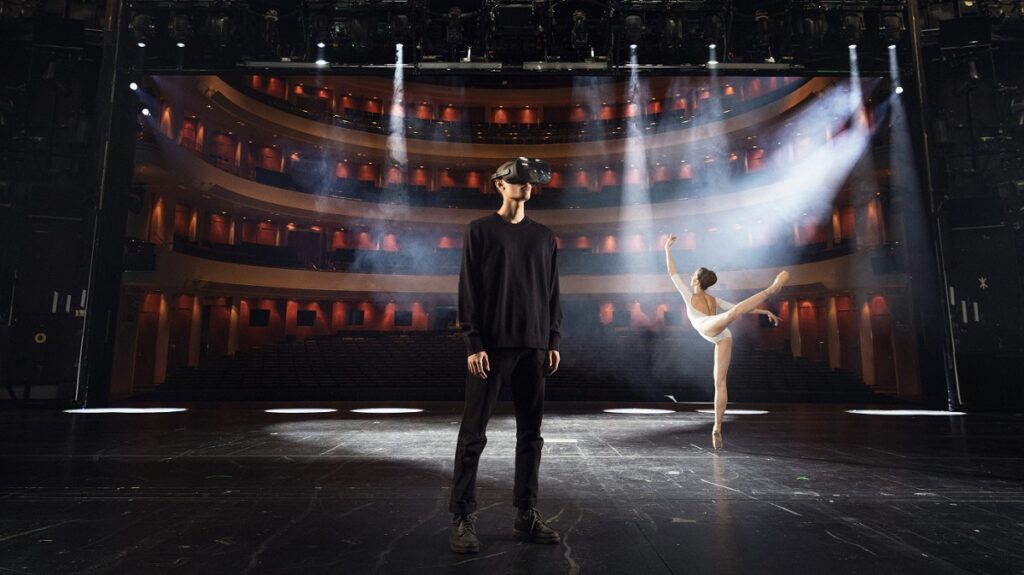 Image of a man using a VR headset on a stage with a ballerina in the background.