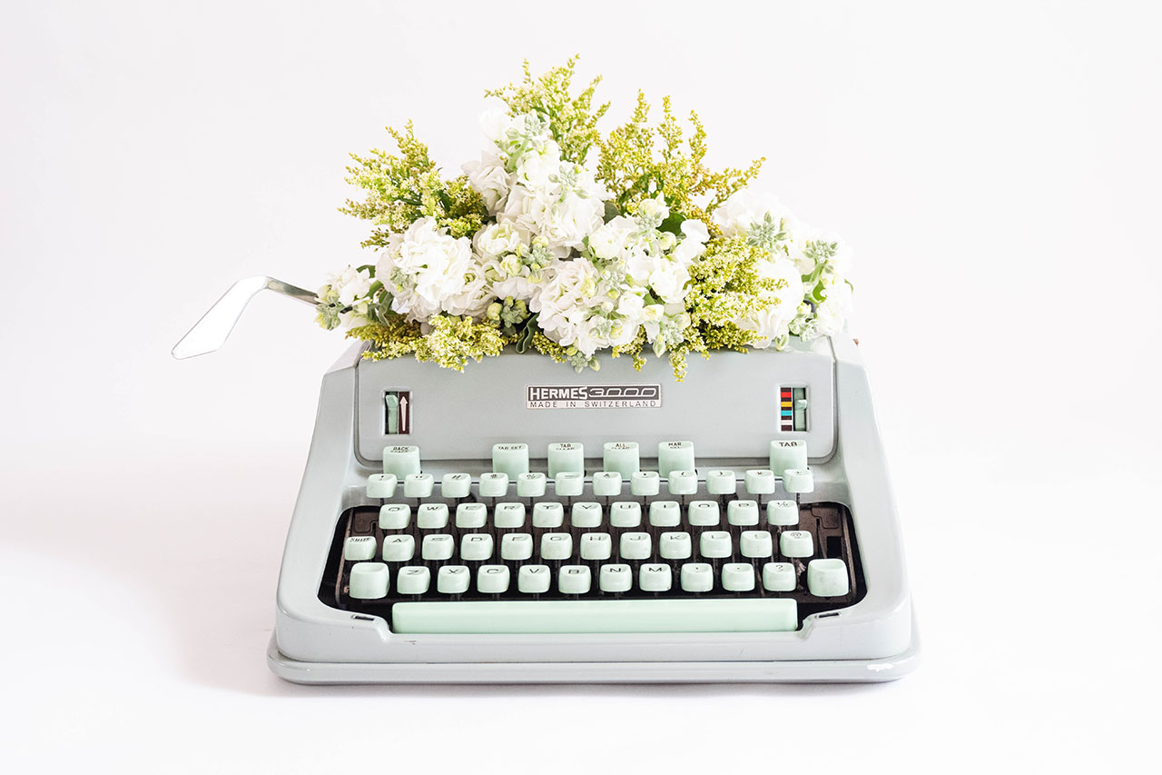 A typewriter with white florals and greenery, © Fiona Murray / Unsplash
