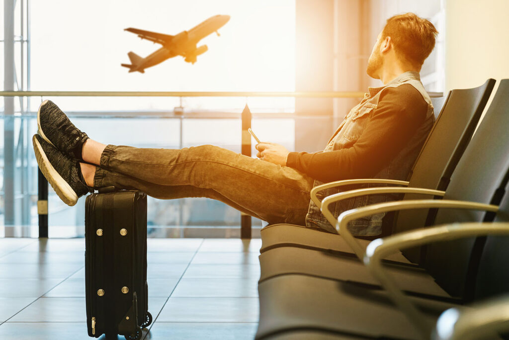 Man sitting on gang chair with feet on luggage looking at airplane,