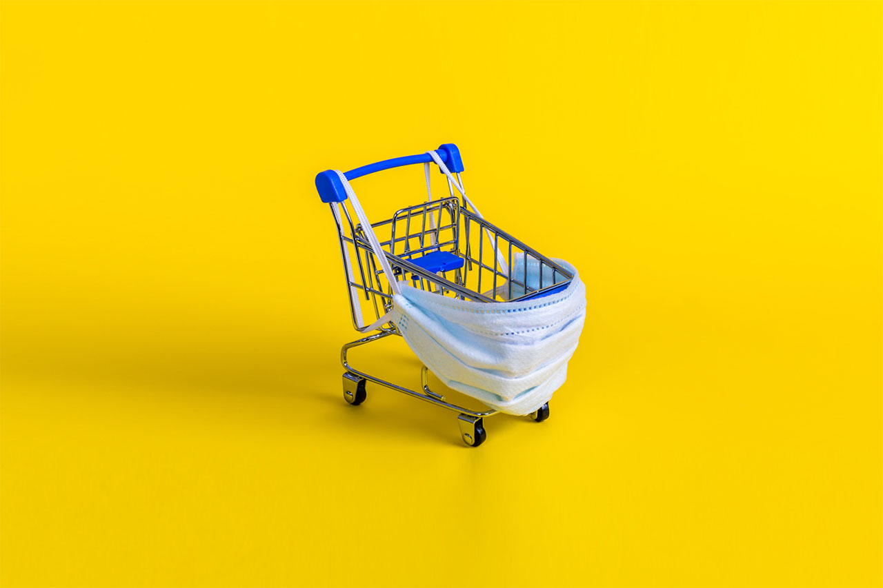 Blue shopping cart with medical mask for virus protection on yellow background.