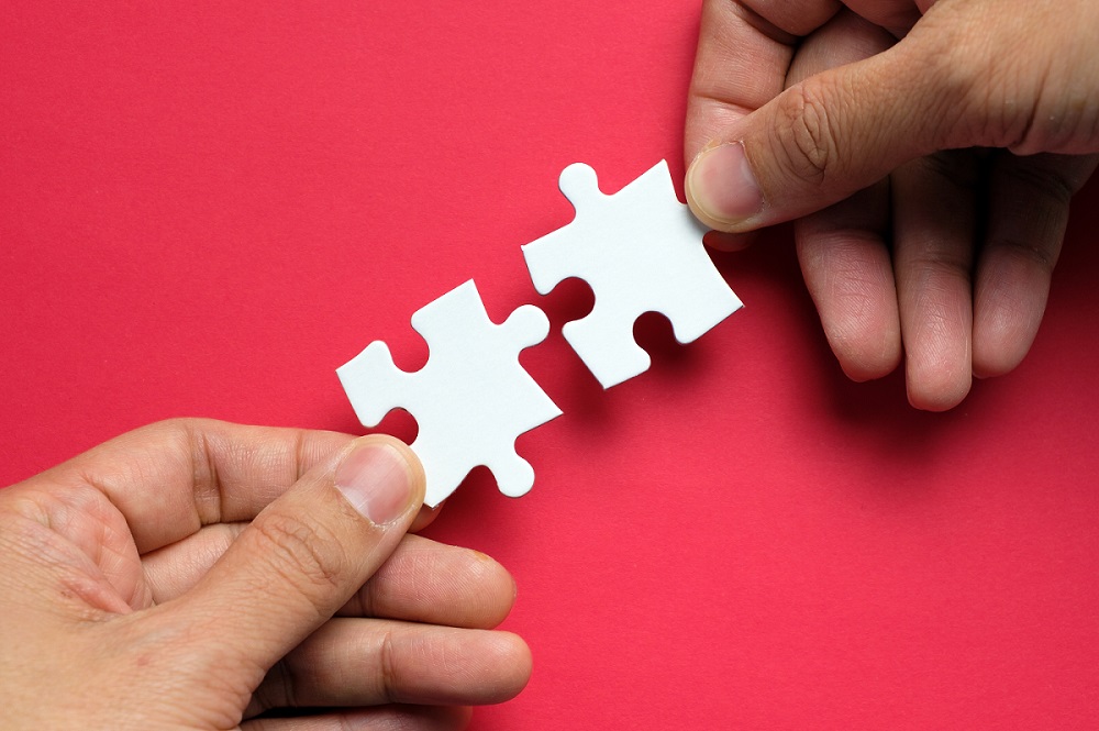Partnership concept with hands putting puzzle pieces together on red background