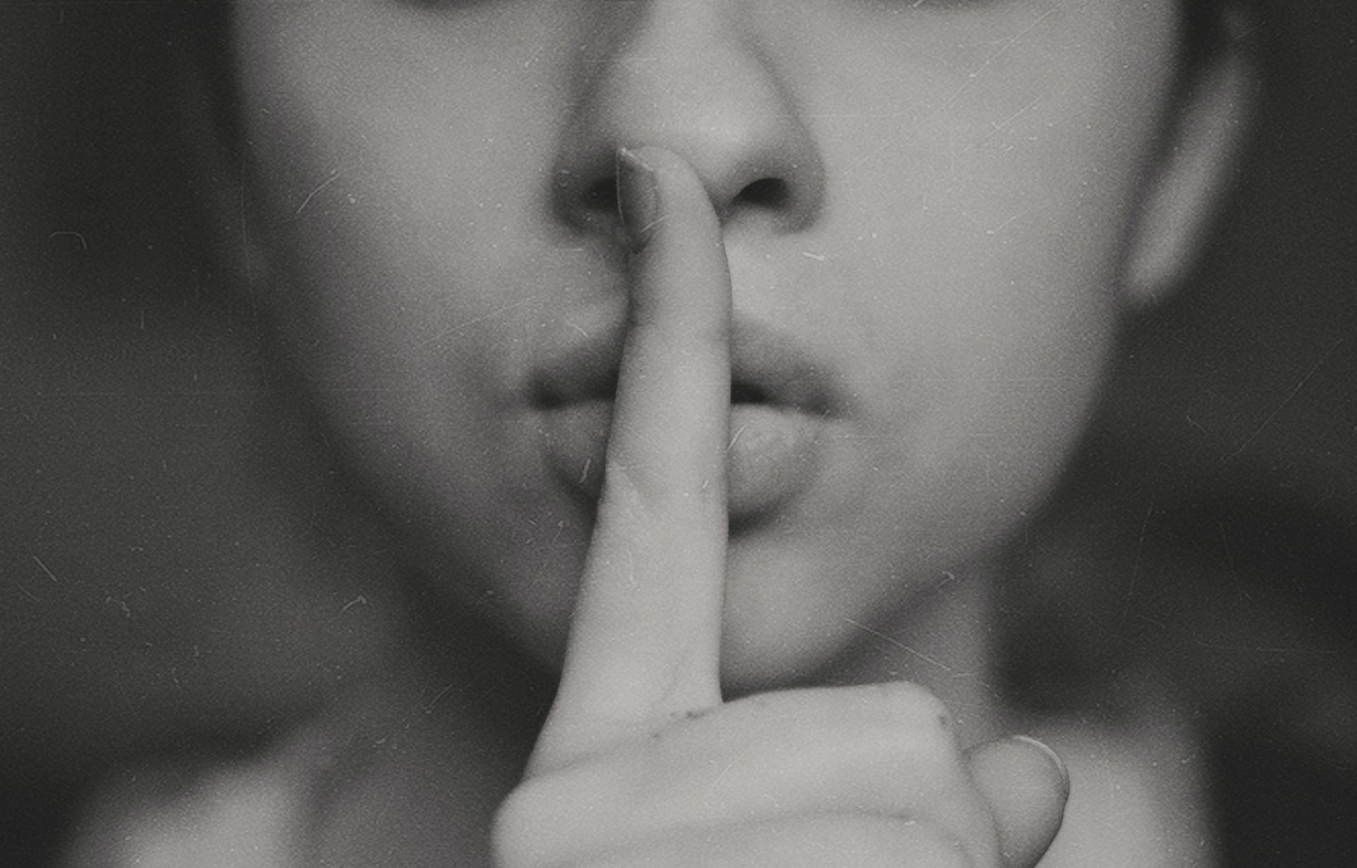 Photo of a woman with her finger to her lips making the sign to be quiet.