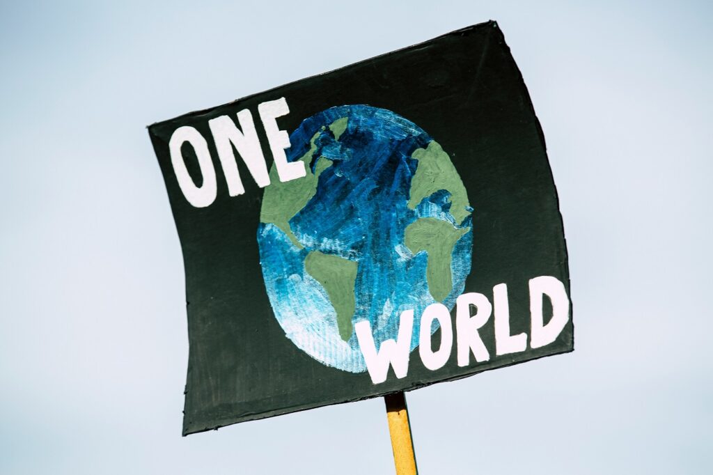 A sign from a protest is held up in the sky featuring a painting of the globe and the words "One World"