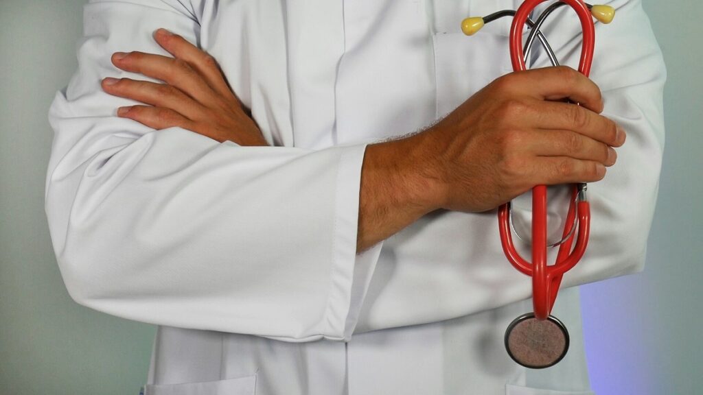 A doctor stands with his arms crossed holding a stethoscope. We do not see his face.