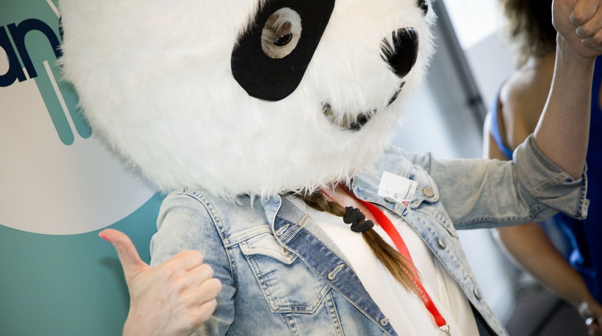 Photo of a woman with a braid wearing a costume Panda head, showing a thumbs up, at a PANDA Network event.