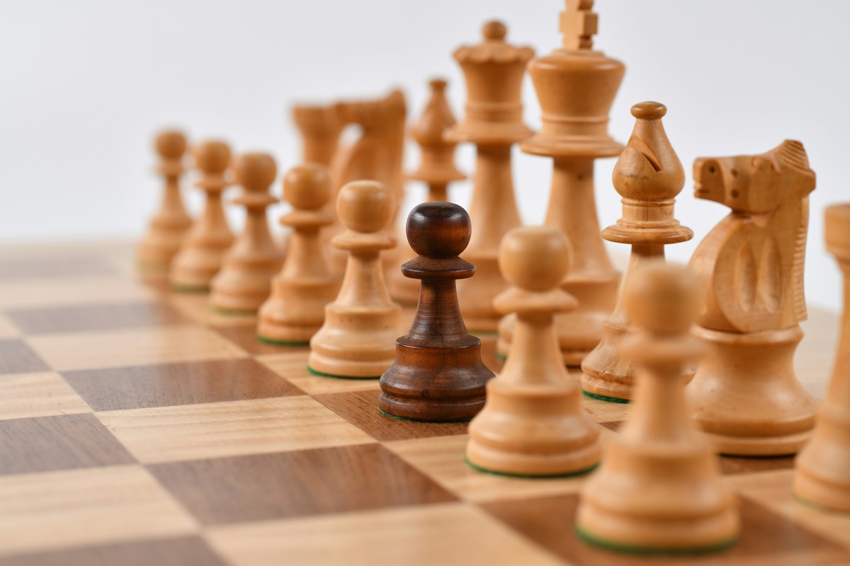 One dark brown chess piece stands out on a board of light brown chess pieces