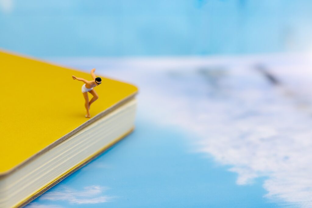 Photo of a male figurine wearing a bathing suit about to dive of a book in to a pretend ocean.