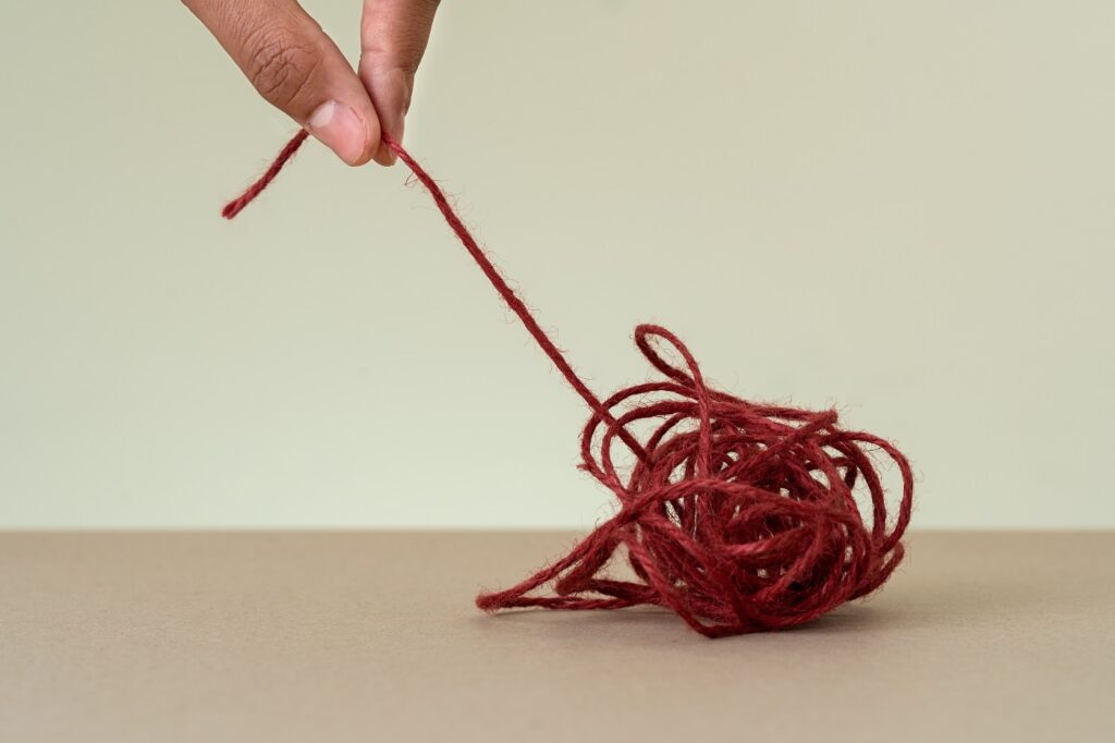 Close up photo of a hand pulling the end of a red ball of string.
