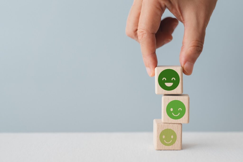 A stack of 3 wooden blocks with happy faces on them that get progressively deeper green and happier as they move up the stack