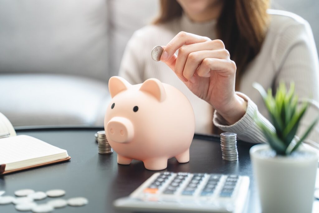 Young woman saving her monthly allowance puts the coin in the piggy bank on the table.