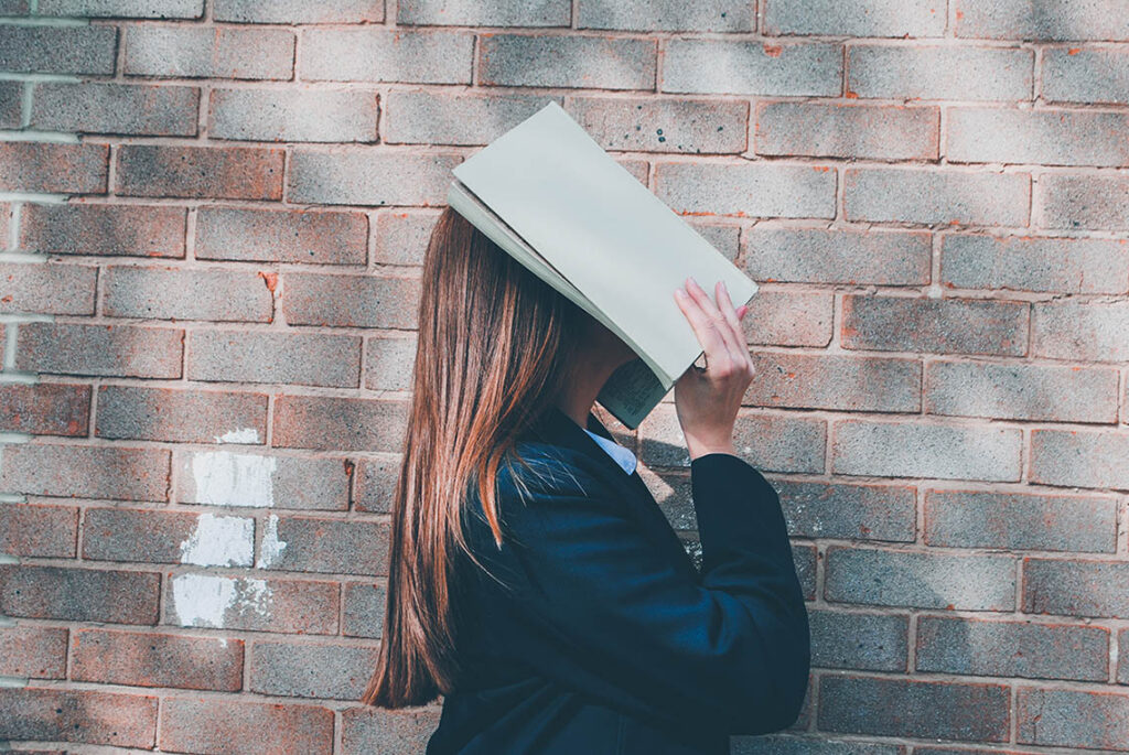 Woman covering her face with an open book, © Siora Photography / Unsplash