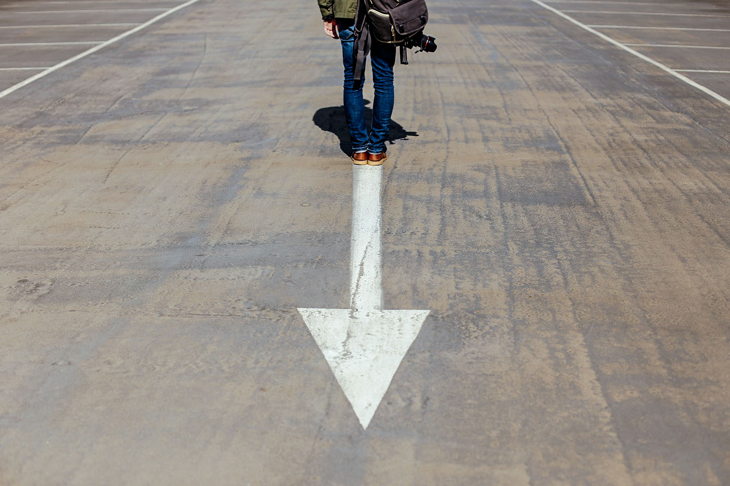 Person standing on arrow sign on road, ©Smart / Unsplash