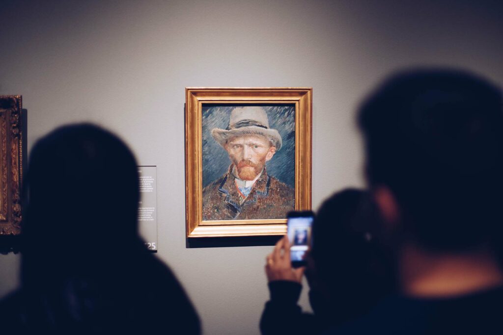 Photo of someone taking a picture of a Vincent VanGogh portrait in a museum.