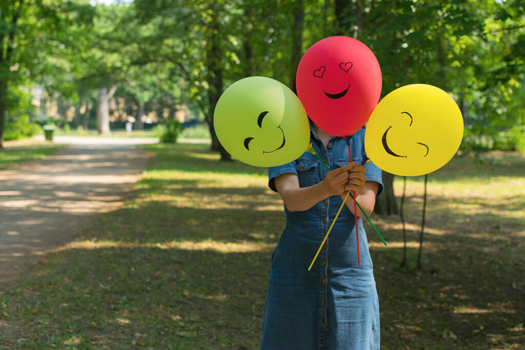 Woman holding air balloons with funny drawn faces, ,© Tatiana / Adobe Stock