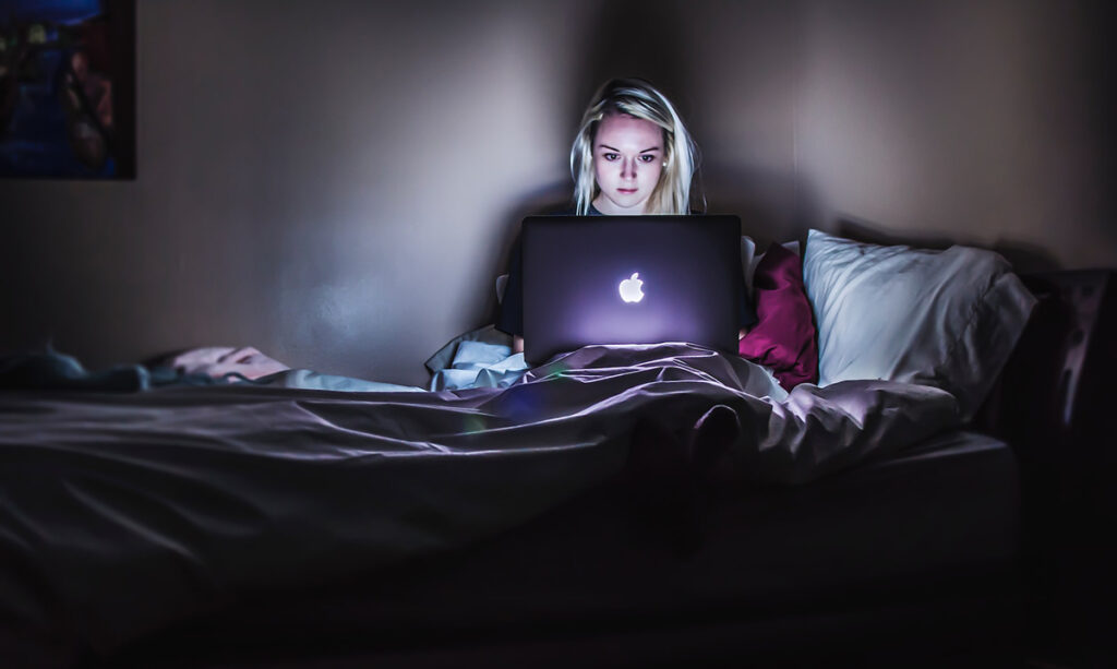 Woman teleworking on a bed in the dark.