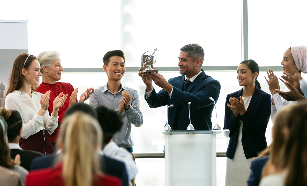 Businessman holding award at podium with colleagues in a business seminar