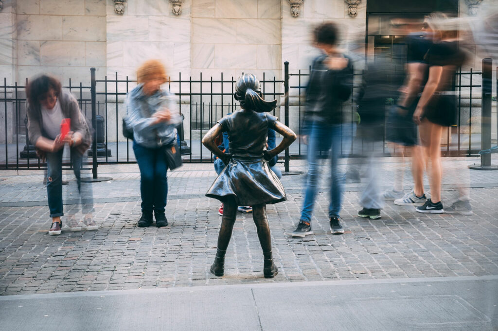 Photo of the Fearless Girl statue in New York City. She is having her photo taken by tourists.