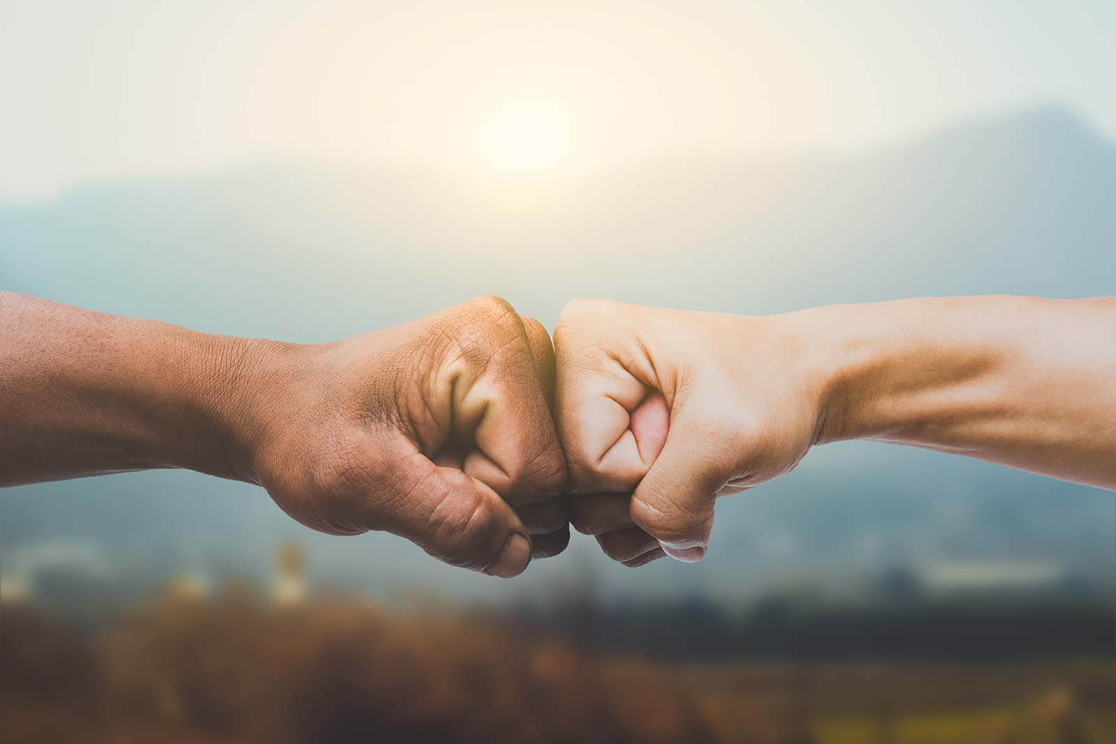 Man giving fist bump in sun rising nature background.