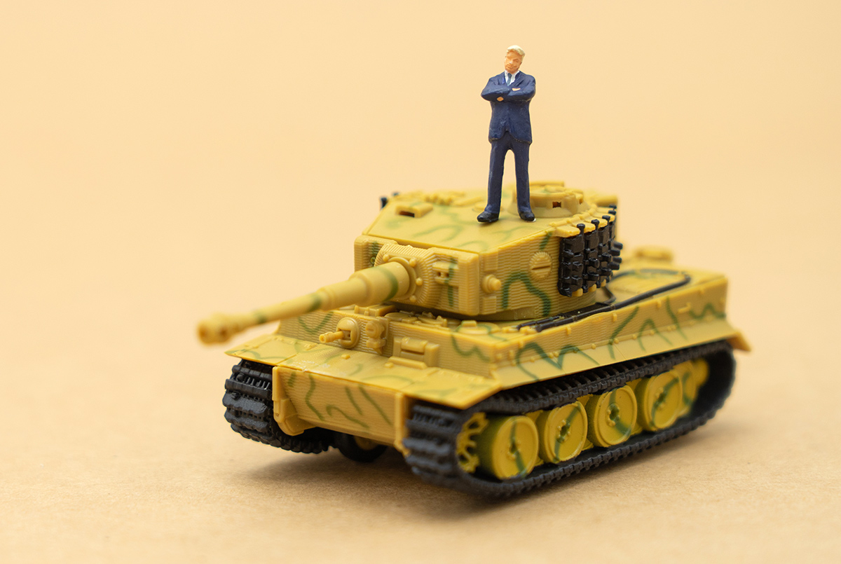 Miniature people businessmen standing with a Tank model on the back Negotiating in business.
